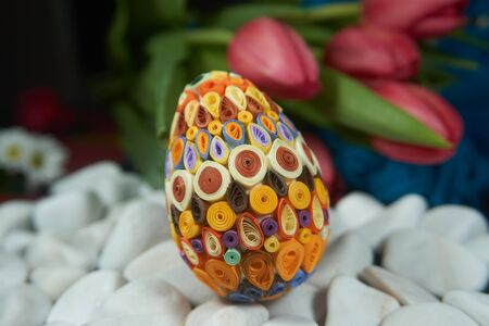 Hand-crafted Easter egg on the surface of white stones near of red tulips. Easter decor, selective focus.の写真素材