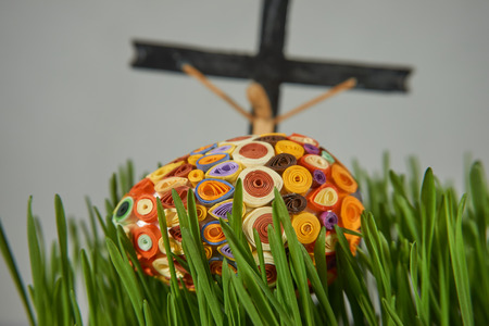 Easter Craft Ideas. The Easter egg decorated with multicolored paper,  placed between frech green wheat germs, cross and crucified in the distance, selected focus.の写真素材