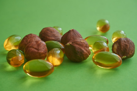 Close up golden color oil capsules and nuts on green background, health care, diet, weight loss, healthy lifestyle concept.の写真素材