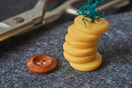 Sewing buttons, thread, scissors on needle punched nonwoven fabric background. Macro view, shallow depth of field.の写真素材