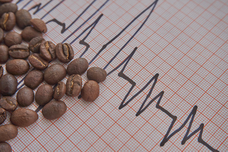 Loose roasted coffee beans on an ECG tracing showing an increased heart beat conceptual of coffee as a stimulant and its health implicationsの写真素材
