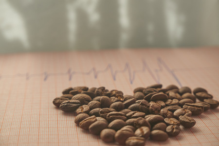 Loose roasted coffee beans on an ECG tracing showing an increased heart beat conceptual of coffee as a stimulant and its health implications,  low angle selective focusの写真素材