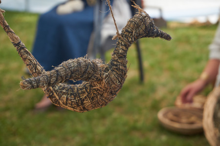Hand-crafted flying bird made from dried grass and straw bound with string with ladies sitting in traditional clothes making them in the backgroundの写真素材