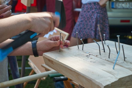 Man hammering a nail into a block of very hard wood which has caused several other nails to bend in a close up of his handsの写真素材