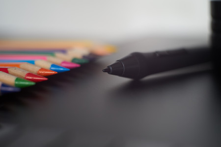 Digital stylus pen on digital graphic tablet for illustrators and designers with coloured pencils in background. Macro view, free space and selective focusの写真素材