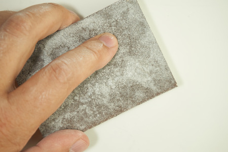 Close view of a hand sanding the wall with a sanding sponge isolated on white. Abrasive tools, DIY, copy space.の写真素材
