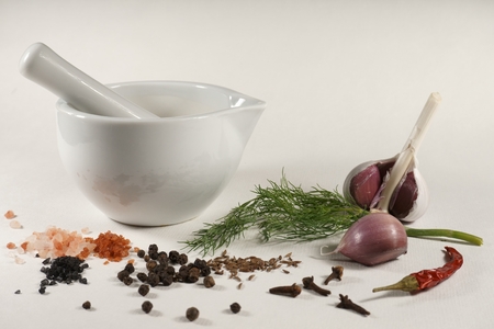 White ceramic mortar and pestle fresh dill garlic cumin seeds Himalayan pink salt Hawaii red aloes salt Hawaii black pearl salt cloves chili pepper black pepper isolated on white backgroundの写真素材