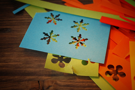 Making homemade bright colorful decorations for a party or Christmas with paper cut outs in a handicraft concept over rustic wood with copy spaceの写真素材