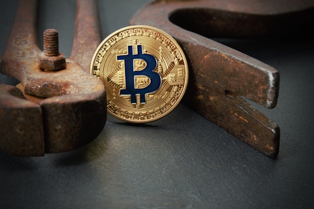 Golden bitcoin trapped between the old rusty vintage claw and nippers. Concept of cryptocurrency...