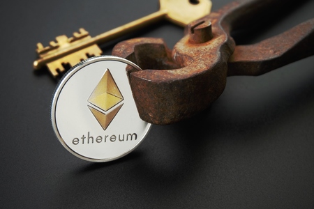 Close up of sheeny Ethereum coin and golden key on rusty vintage nippers. Cryptocurrency key code, secure Ethereum wallets concept. Black background with selective focus and copy spaceの写真素材
