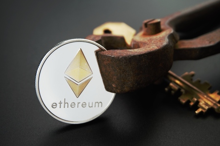 Close up of sheeny Ethereum coin and golden key on rusty vintage nippers. Cryptocurrency key code, secure Ethereum wallets concept. Black background with selective focus and copy spaceの写真素材