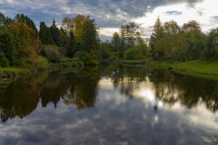 Fall season start idyllic lake reflections of fall foliage. Autumn scenery with cloudy sunset and reflection on the calm watersの写真素材