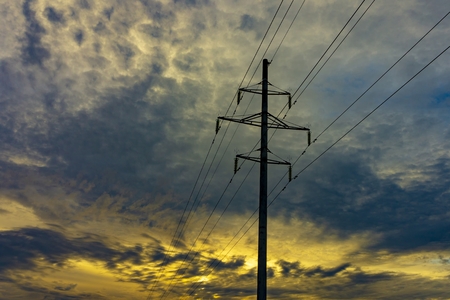 High tension electricity power lines and pole silhouetted against a colorful sunset sky with cloud cover and copy spaceの写真素材