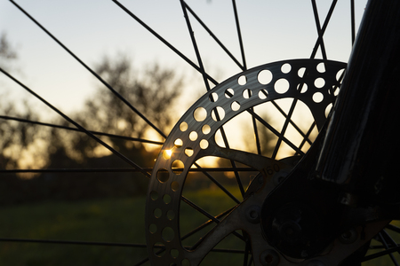 Cropped view of spokes on a bicycle wheel looking through to a green field at sunsetの写真素材