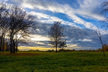 Meadows and autumn trees against colorful evening sky decorated with clouds, fades away to the dark of nightの写真素材