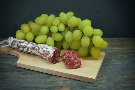 Sliced dry cured Fuet sausage and green grapes on wooden cutting board