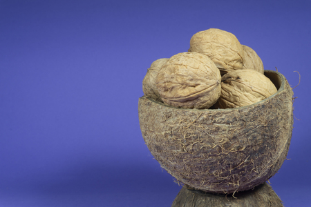 Pile of whole common walnuts with shells in natural coconut shell cup on bright blue background