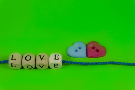 Red and blue heart shaped buttons and word Love on blocks threaded on strings over a colorful green background for romantic or Valentines concepts with free copy space for textの写真素材