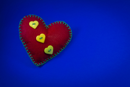 One handmade red felt stitched toy heart on blue background, close up, high angle view with free copy space. Love, relationship, Valentines Day, broken heart conceptの写真素材