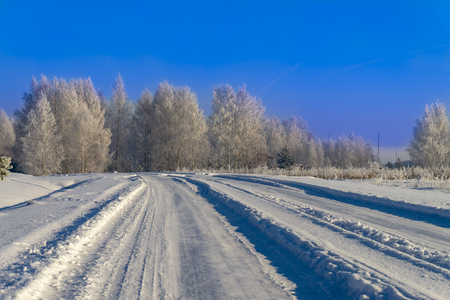 Snow covered winter road lined with frosty white trees receding into the distance on a sunny day with clear blue sky in a scenic seasonal landscapeの写真素材