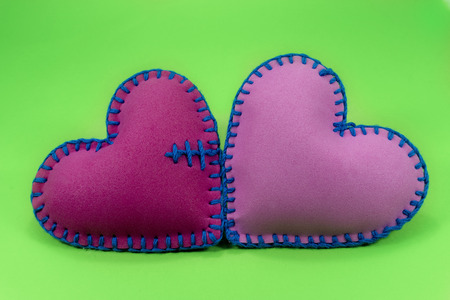 Hand stitched foam sheet red and pink toy hearts over a colorful green background for romantic, relationship, Valentines Day, broken heart, love conceptの写真素材