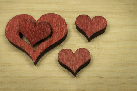 Laser cut red wooden heart shapes on light wood surface background for love and romance concepts with free copy space for textの写真素材