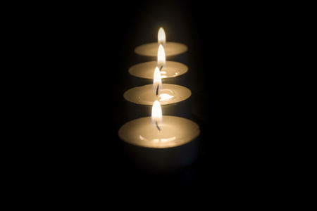 Close up shot of several lined up tea light candles in the dark with focus changing from back to the...