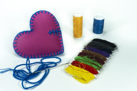 Hand stitched textile heart and colored sewing threads isolated on white background for romantic...