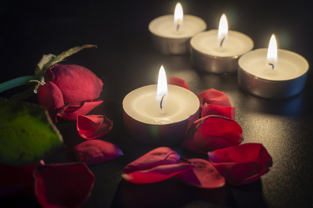 Four tea candles and red rose petals in the dark with shallow depth of focusの写真素材