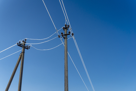 Two electric line poles with frozen wires in winter, viewed from low angle against clear blue skyの写真素材