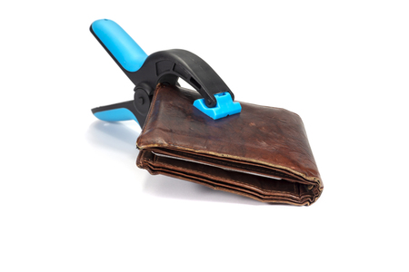 Old worn leather wallet held by an industrial clamp over a white background in a conceptual image of financial security or controlling spendingの写真素材