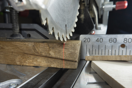Teeth on a circular power saw in close up with assorted blocks of wood and a metal scale for cutting lengths in a woodworking workshopの写真素材