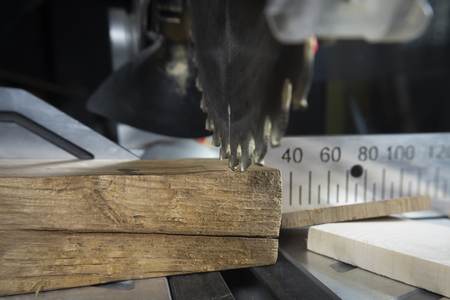 Teeth on a circular power saw in close up with assorted blocks of wood and a metal scale for cutting lengths in a woodworking workshopの写真素材