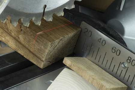 Teeth on a circular power saw in close up with assorted blocks of wood and a metal scale for cutting lengths in a woodworking workshopの写真素材