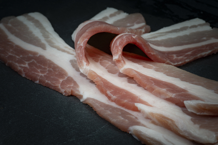 Close up raw dry-cured back bacon on a dark stone serving plateの写真素材
