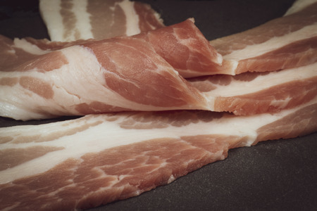 Close up raw dry-cured back bacon on a dark stone serving plateの写真素材