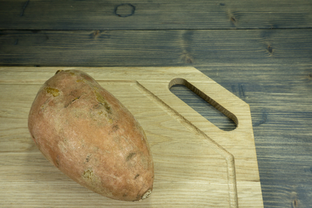 Whole sweet potato Ipomoea batatas in close up on a wooden cutting board on dark rustic table backgroundの写真素材