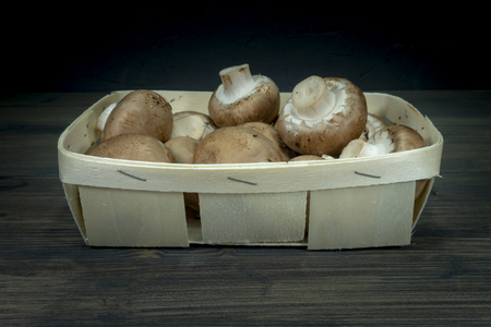 Fresh whole crimini (Baby Bella) mushrooms in the wooden basket on dark rustic table backgroundの写真素材
