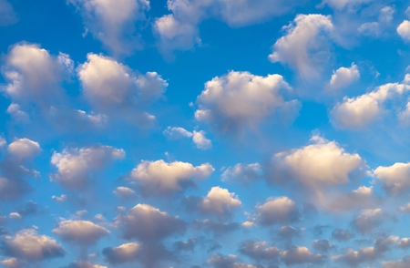 Blue sky background with pretty fluffy white clouds tinged with color in evening light with side vignette in a full frame viewの写真素材