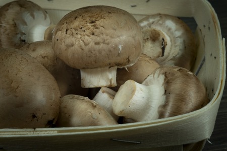 Fresh whole crimini (Baby Bella) mushrooms in the wooden basket on dark rustic table backgroundの写真素材