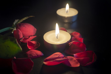 Two tea candles, red rose petals with shallow depth of focus with reflection on black backgroundの写真素材