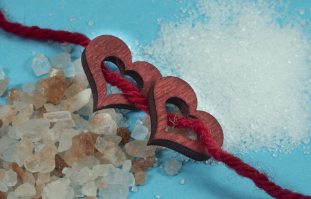 Two wooden decorative hearts threaded on red rope with a pile of rough salt crystals on one side and fine crushed salt or sugar grains on the other in a conceptual imageの写真素材