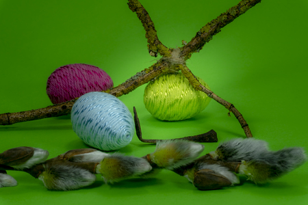 Handmade Easter eggs, soft willow buds and cross of twigs in close-up on green background. Christian symbols of Palm Sunday or Easterの写真素材
