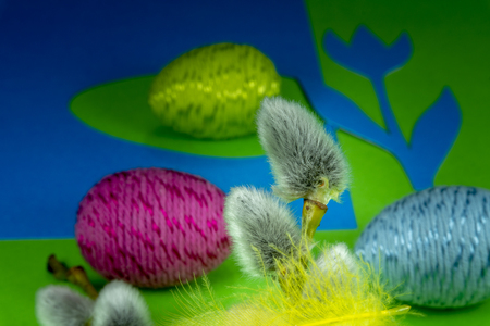 Willow buds, Easter eggs and feather in close-up as a set of decoration on spring theme in Christianity, placed on green background with flower cutout of blue paperの写真素材