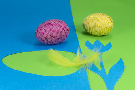Easter eggs and feather in close-up as a set of decoration on spring theme in Christianity, placed on green background with flower cutout of blue paperの写真素材