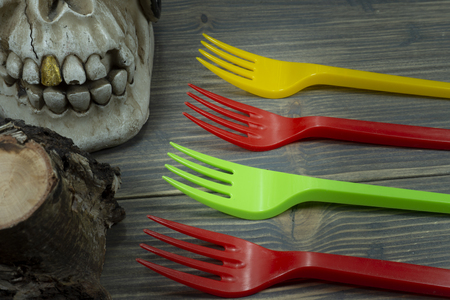 Pirate skull toy and colorful plastic forks on wooden background in close-up. Plastic waste problem conceptの写真素材