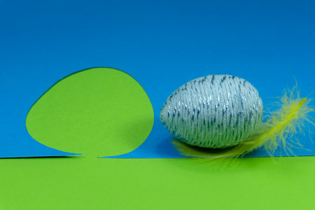 Easter egg and feather in close-up as a set of decoration on spring theme in Christianity, placed on green background with flower cutout of blue paperの写真素材