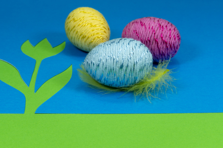 Easter egg and feather in close-up as a set of decoration on spring theme in Christianity, placed on green background with flower cutout of blue paperの写真素材
