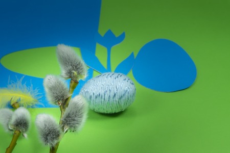 Willow buds, Easter eggs and feather in close-up as a set of decoration on spring theme in Christianity, placed on green background with flower cutout of blue paperの写真素材