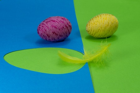 Easter egg and feather in close-up as a set of decoration on spring theme in Christianity, placed on green background with flower cutout of blue paperの写真素材